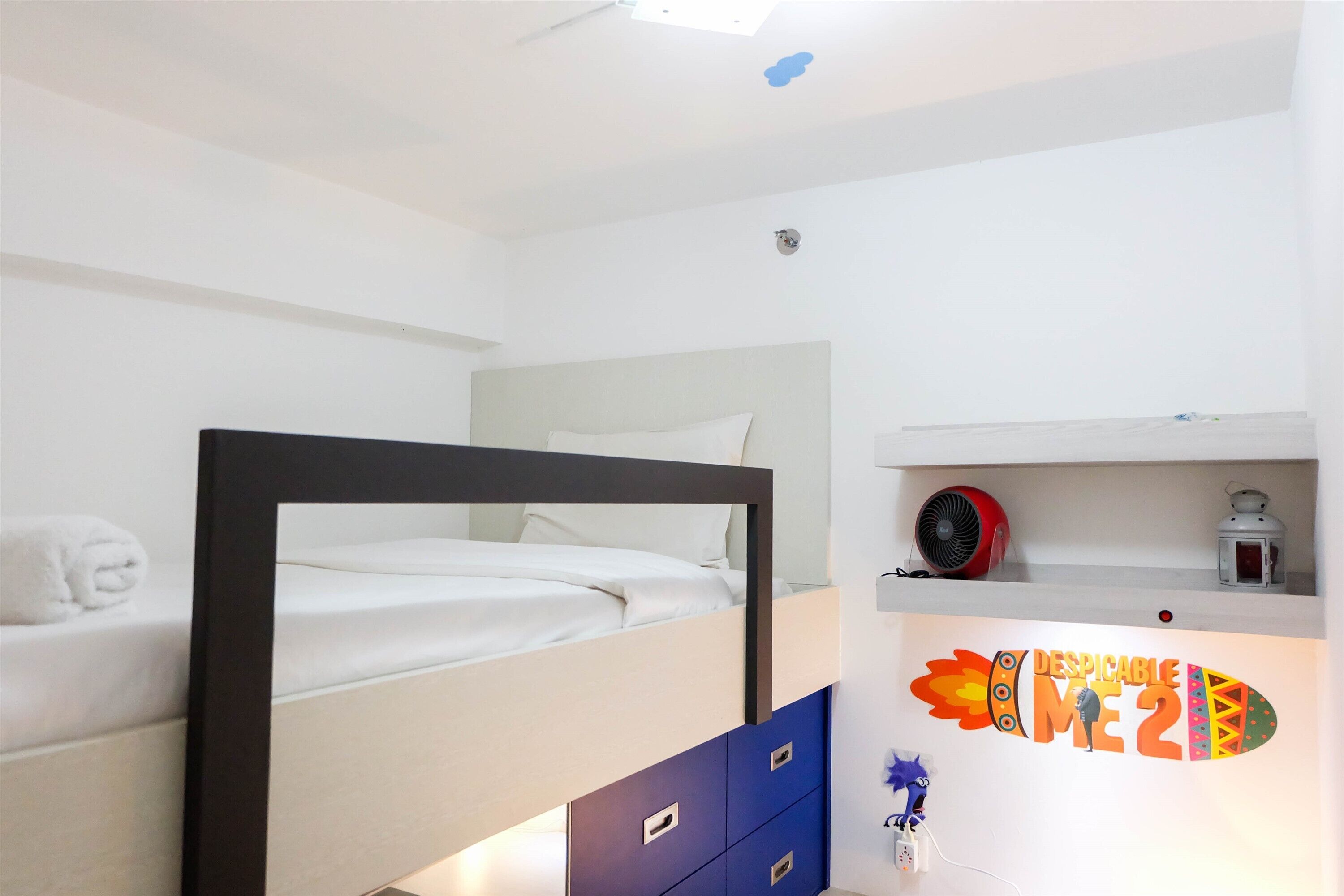 A bedroom with a bunk bed, a small shelf with a fan and a lantern, and a wall decoration.