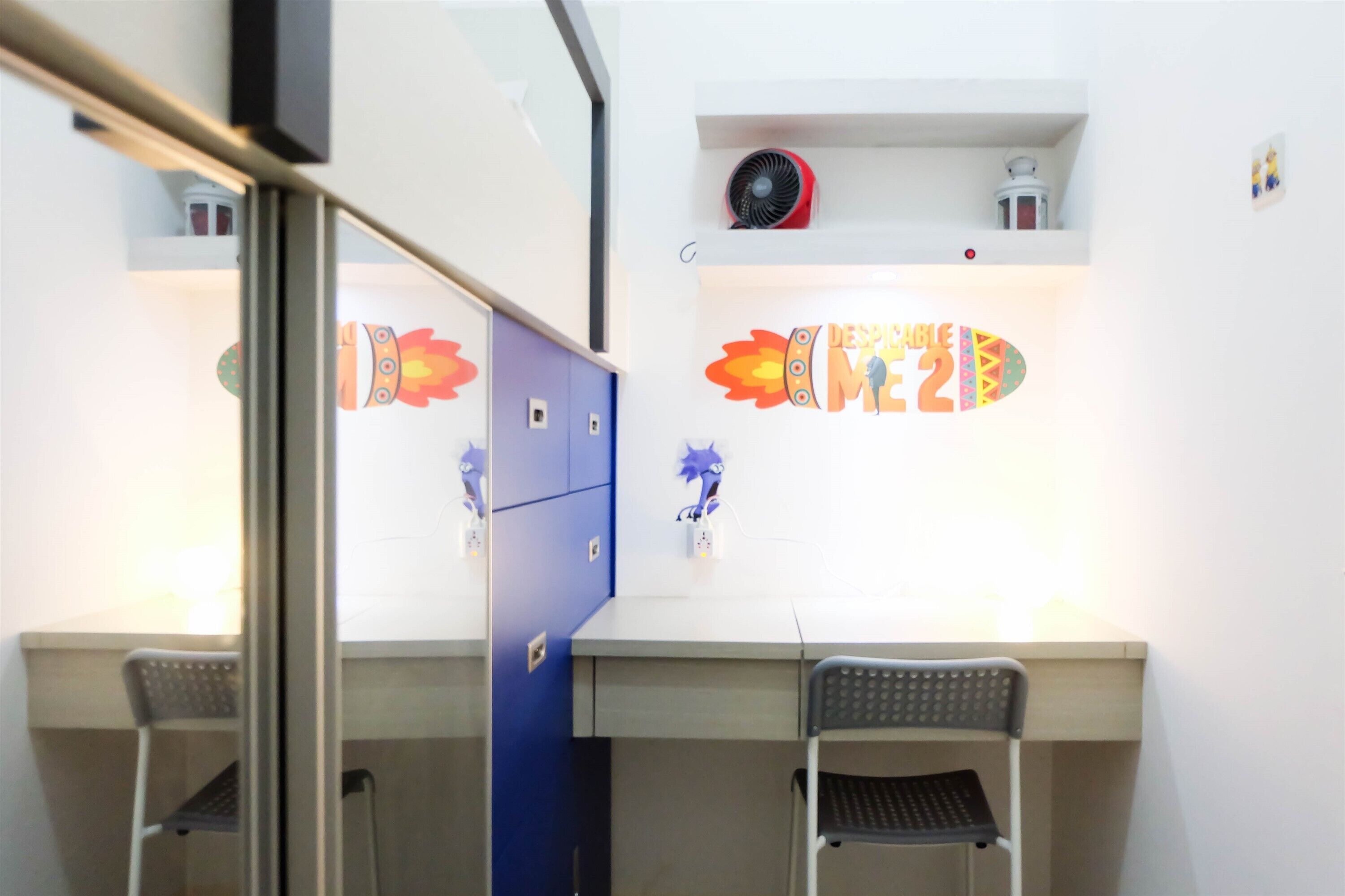 A room with a desk, two chairs, a blue filing cabinet, and a wall decoration.