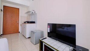 A compact living space with a television, a small refrigerator, and a kitchenette area. - Simple Furnished Studio Apartment at Maple Park (Jakarta)
