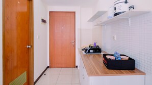 A small kitchen with a wooden door, a countertop with a coffee maker, and a box of bottled water. - Simple Furnished Studio Apartment at Maple Park (Jakarta)