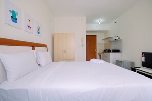 A hotel room with a large bed, a wooden wardrobe, a kitchenette, and a TV. - Simple Furnished Studio Apartment at Maple Park (Jakarta)
