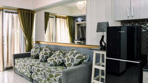 A modern living room with a sofa, a black refrigerator, and a large mirror. - Chic and Cozy 1BR Apartment at H Residence near MT Haryono (Jakarta)