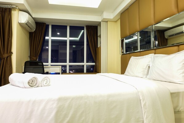 A hotel room with a large bed, a window with curtains, an air conditioning unit, and a mirror on the wall.