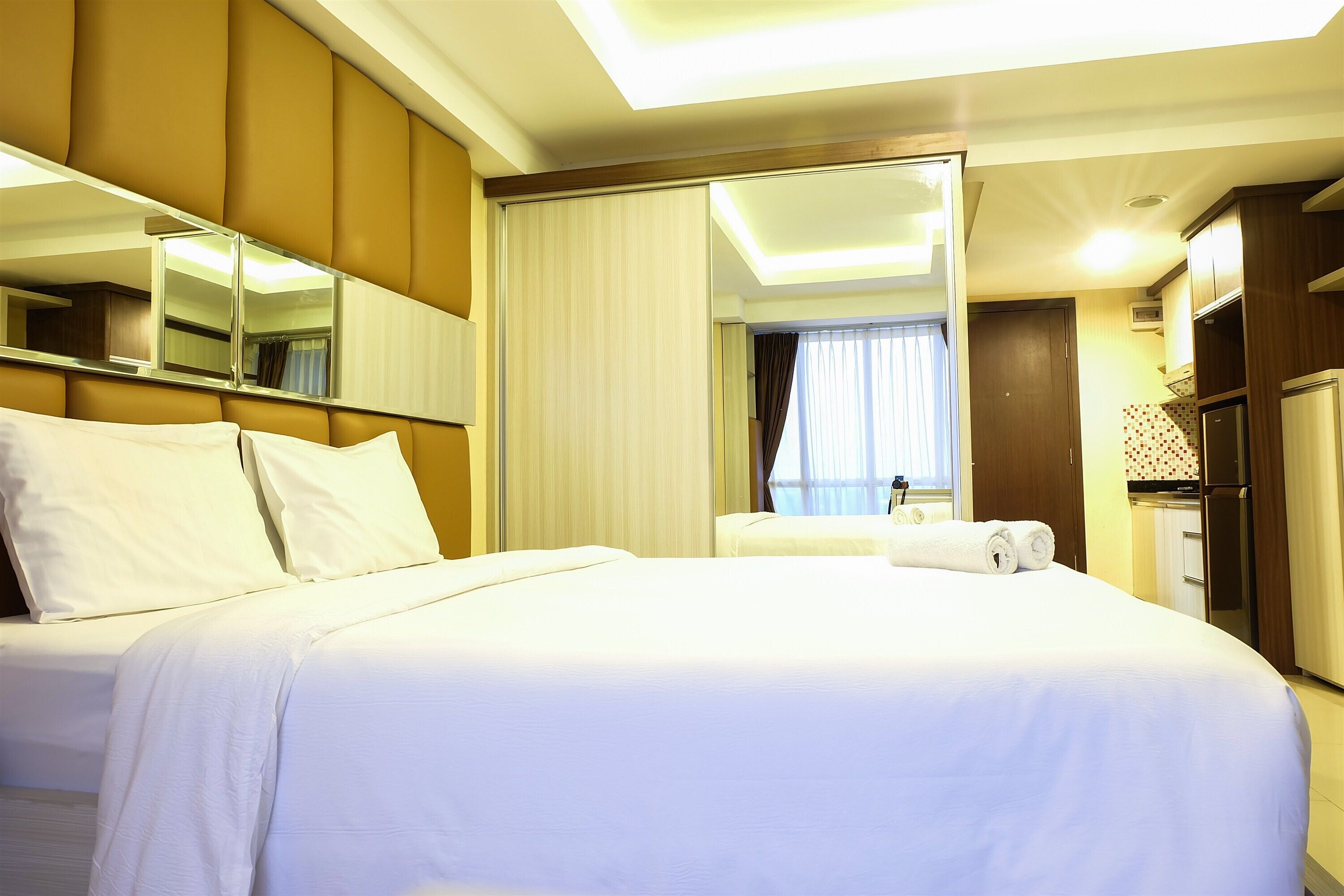 A hotel room with a large bed, a mirror, a wardrobe, and a bathroom visible through a sliding door.