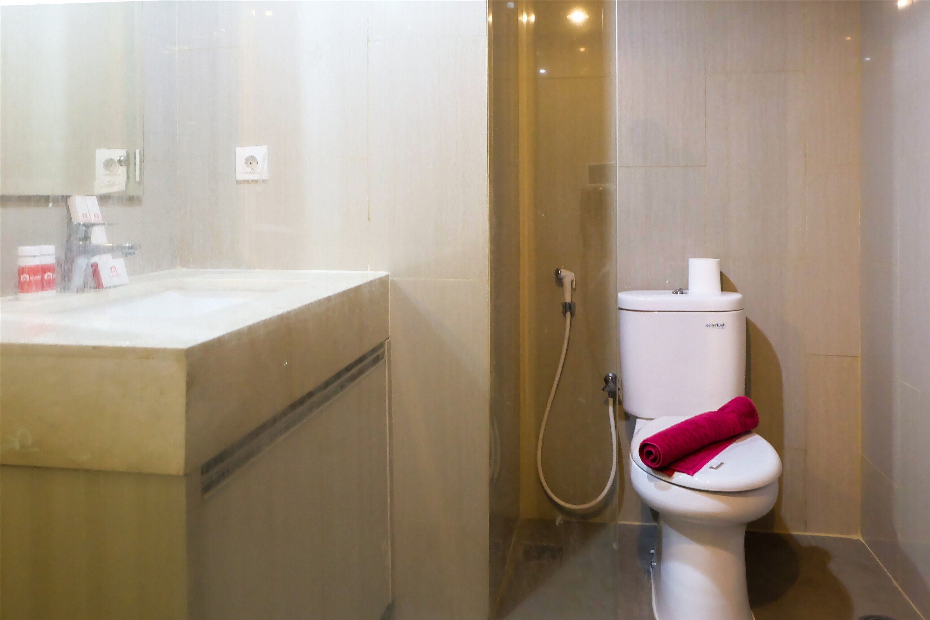 A modern bathroom with a white sink, a toilet with a pink towel, and a shower area.