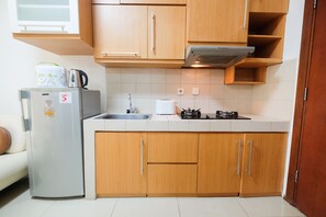 A compact kitchen with wooden cabinets, a stainless steel refrigerator, a microwave, and a gas stove. - Great Choice and Strategic 1BR Apartment at Thamrin Residence (Jakarta)