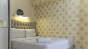 A neatly made bed with white linens and a rolled towel, a tufted headboard, and a wall clock above it. - Nice and Comfy 2BR Bassura City Apartment near Mall (Jakarta)