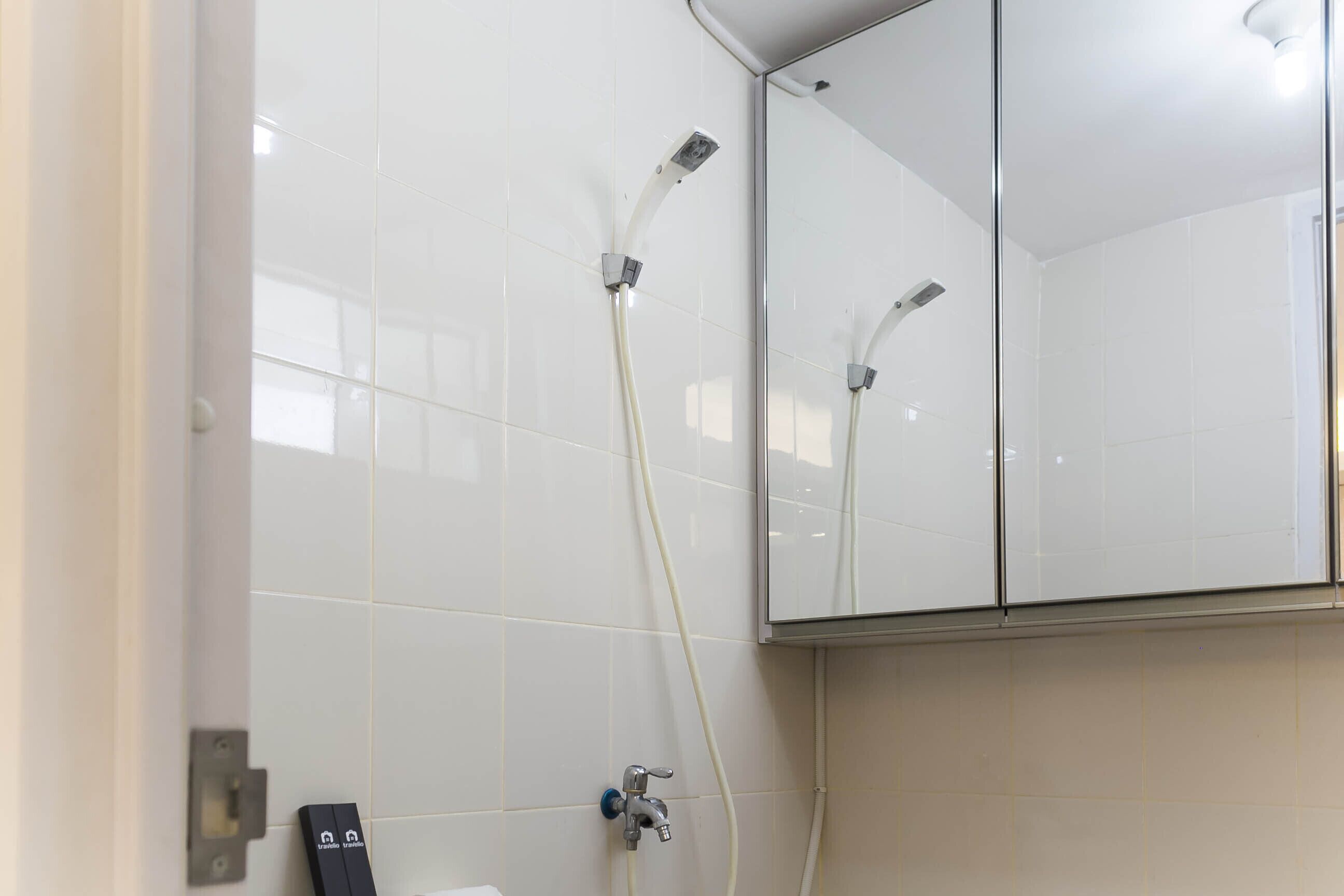 A bathroom with white tiles, a shower with a handheld showerhead, and a mirror above the sink.