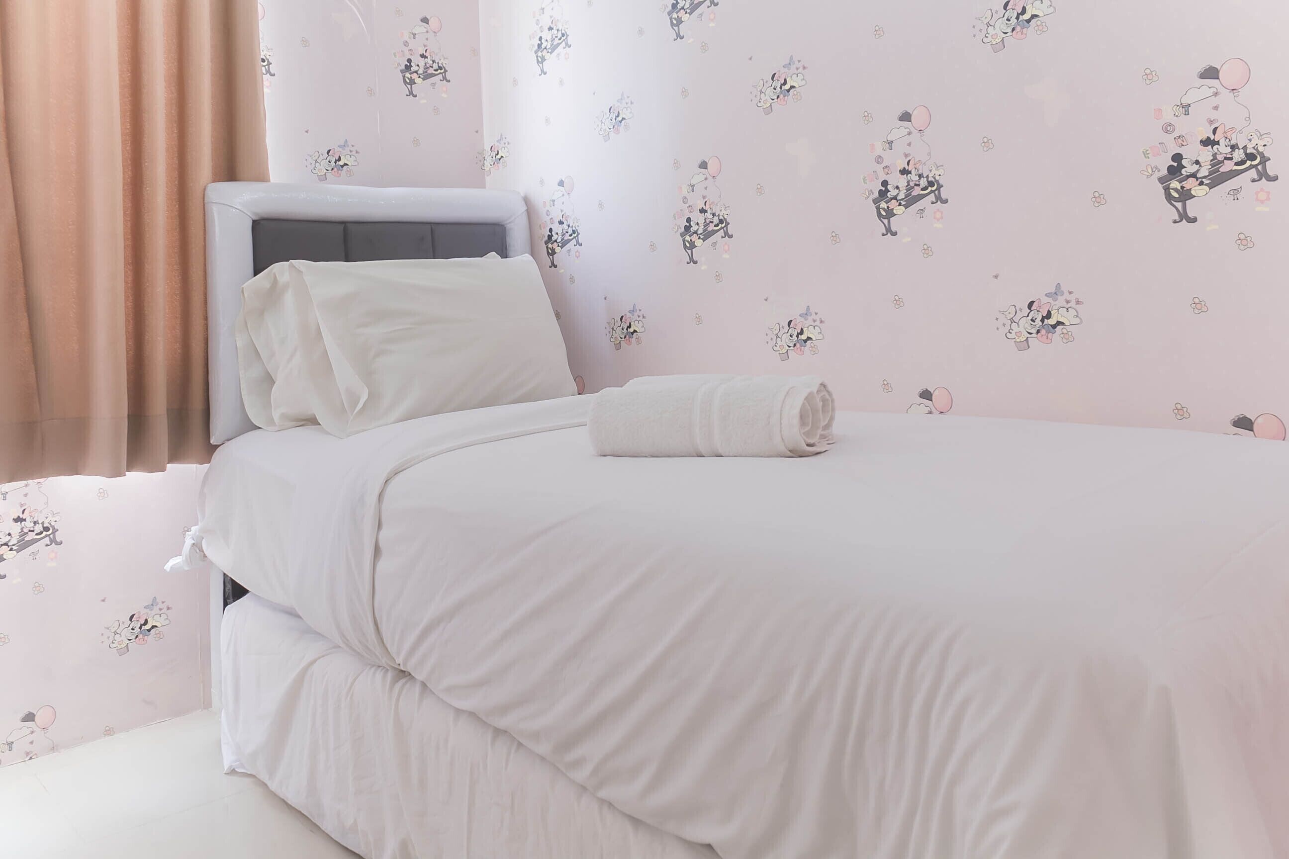 A neatly made bed with white bedding and a folded towel, a grey headboard, and a wall with floral wallpaper.