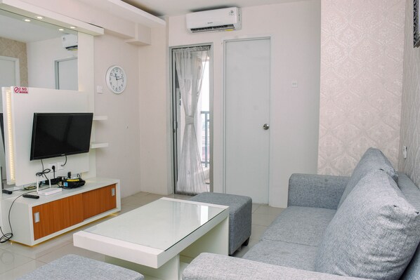 A modern living room with a flat-screen TV, a glass coffee table, grey sofas, and a white cabinet.