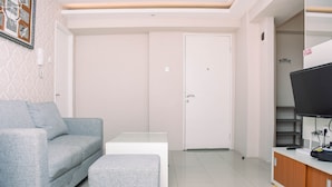 Una sala de estar moderna con un sofá gris, un reposapiés a juego, una mesa de centro blanca y un televisor sobre un mueble de madera.