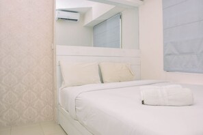 A neatly made bed with white bedding and pillows, a white air conditioning unit mounted on the wall, and a patterned wallpaper on the wall.