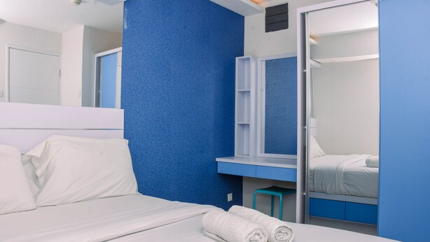 Una habitación de hotel moderna con una cama grande, un muro azul decorativo, un espejo y un armario.