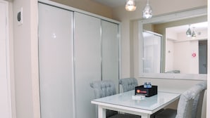 Habitación de hotel con mesa de vidrio, sillas tapizadas en gris, un minibar y un espejo grande.