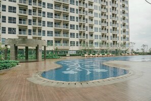 Una piscina amb una font, envoltada d'un pont de fusta, i un edifici residencial gran al fons.