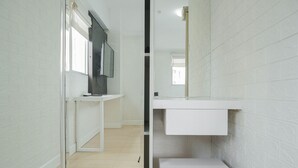 A narrow hallway with white brick walls, a white door, and a white counter with a flat-screen TV. - Best Location 2BR at The Wave Kuningan Apartment (Jakarta)