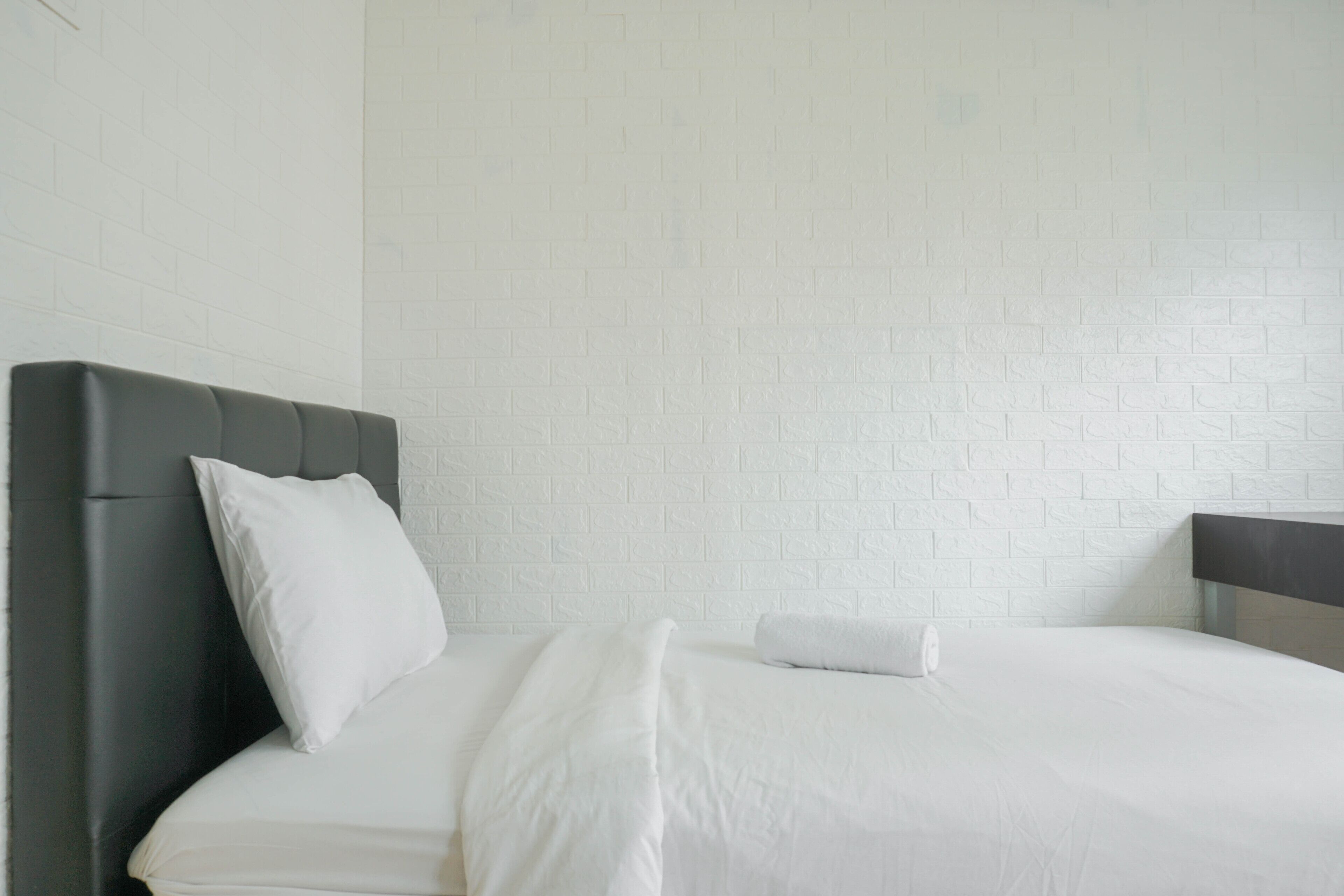 Una habitación de hotel moderna con pared de ladrillo, cabecero oscuro y cama con ropa blanca bien tendida.