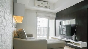 A modern living room with a grey sofa, a flat-screen TV, and a white entertainment unit. - Best Location 2BR at The Wave Kuningan Apartment (Jakarta)