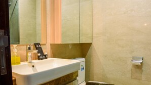 Une salle de bain avec un lavabo blanc, une serviette sur les toilettes et un miroir au-dessus du lavabo.