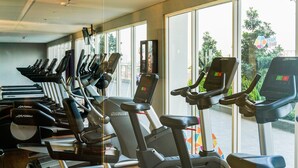Une salle de sport équipée de nombreux tapis de course et d’elliptiques disposés en rangées, et de grandes fenêtres offrant une vue sur l’extérieur.