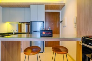 A modern kitchen with a glass countertop, stainless steel appliances, and wooden accents. There are two wooden stools at the counter.