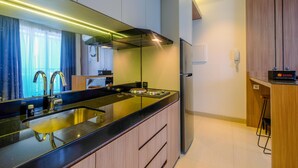 A modern kitchen with a black countertop, stainless steel sink, and a built-in oven. There is a wooden cabinet and a stainless steel refrigerator. - Fabulous 1BR Apartment at The Newton Ciputra World 2 (Jakarta)