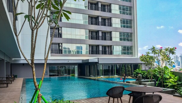 A modern building with a rooftop pool, surrounded by lush greenery and furnished with outdoor seating. - Fabulous 1BR Apartment at The Newton Ciputra World 2 (Jakarta)