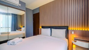 A hotel room with a large bed, a bedside table, a mirror, and a wall-mounted air conditioner. - Fabulous 1BR Apartment at The Newton Ciputra World 2 (Jakarta)