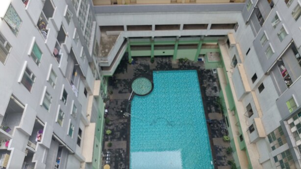 A rooftop pool with a circular hot tub, surrounded by a multi-story building with balconies.