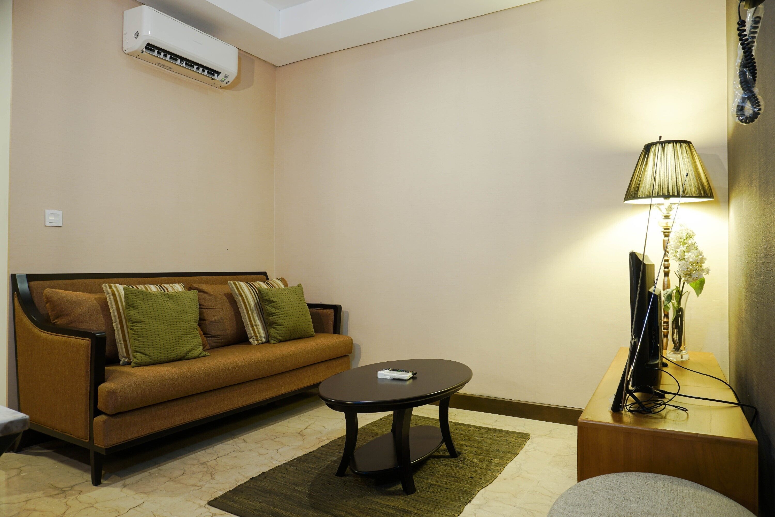 A living room with a sofa, a coffee table, a lamp, and a flat-screen TV on a wooden stand.