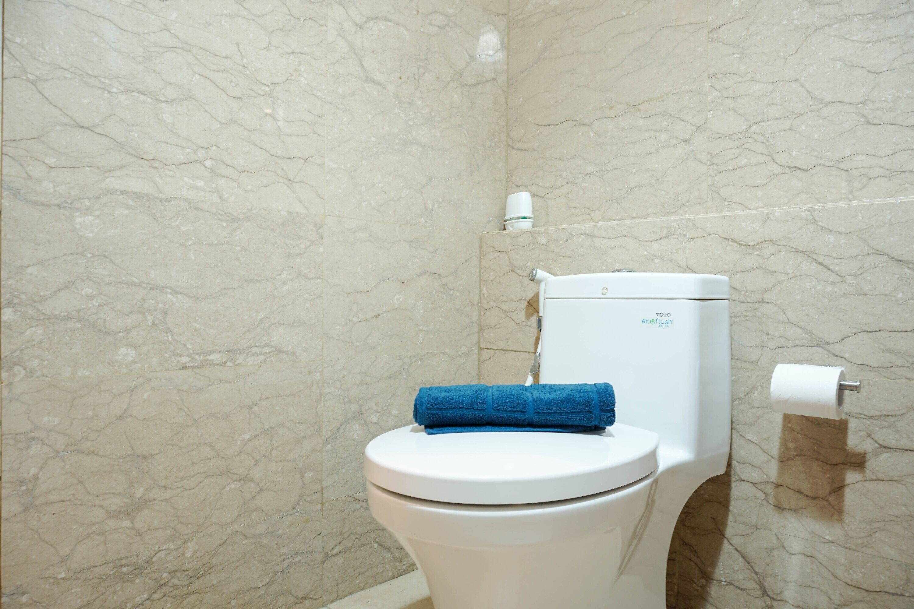 A bathroom with a toilet, marble walls, and a blue towel on the seat.
