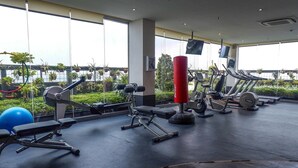Ett gym med olika typer av träningsutrustning, stora fönster och utsikt över grönområden utanför.