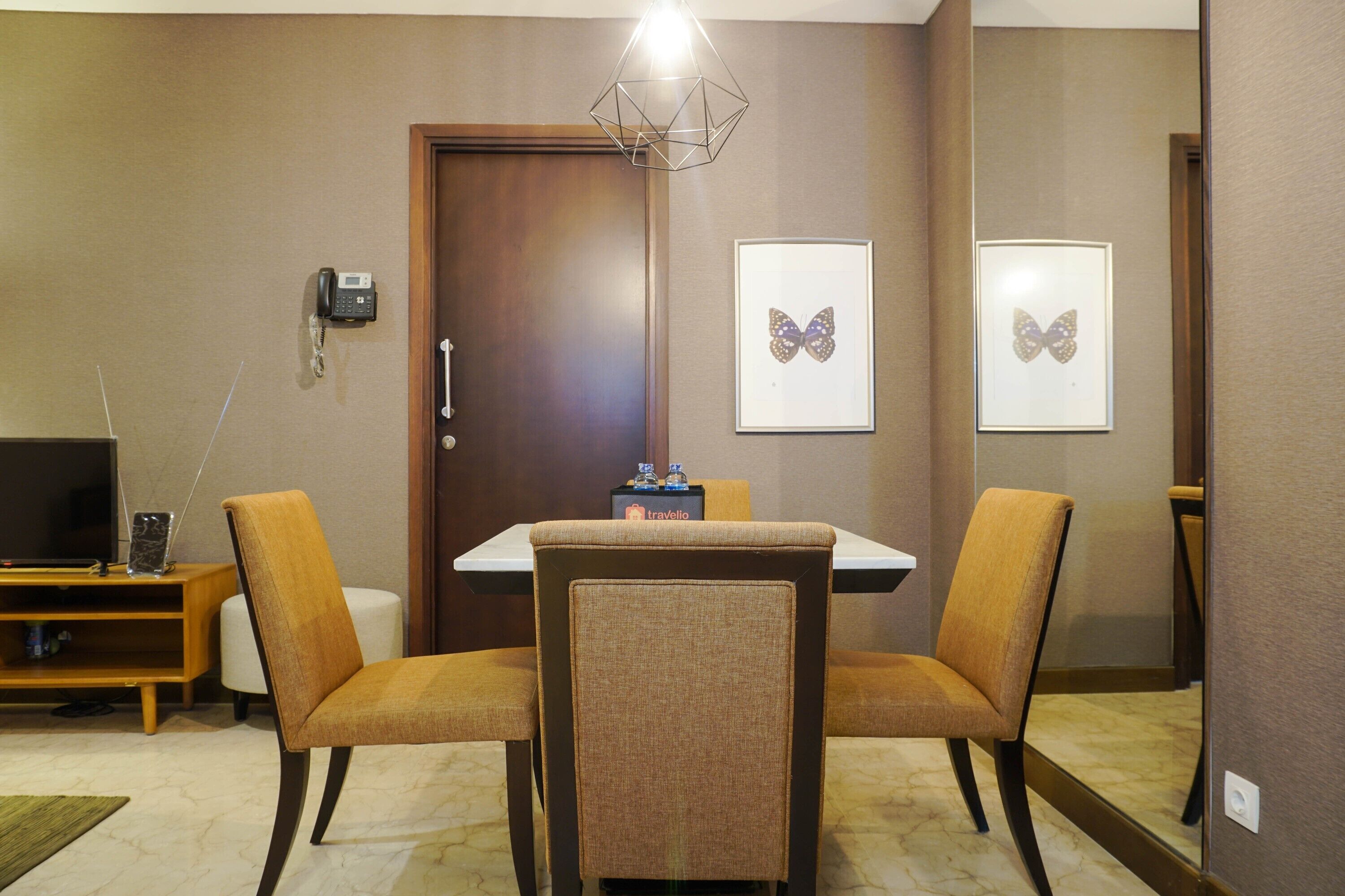 Habitación de hotel con puerta de madera, dos sillas, una mesa, televisor y teléfono en la pared.