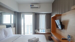 Una habitación de hotel con una cama, un televisor montado en la pared, una ventana con persianas y un equipo de aire acondicionado.