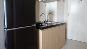 Cocina compacta con refrigerador negro, armarios de madera y pileta de acero inoxidable.