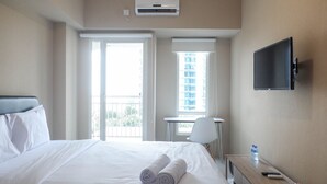 Habitación de hotel con cama, escritorio, silla, televisor y balcón con vistas a edificios.