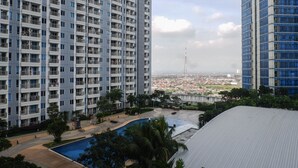 Un edificio residencial alto con varios balcones, una piscina y vistas a un paisaje urbano al fondo.