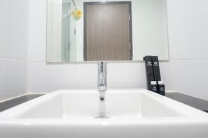 A white bathroom sink with a mirror above it, a wooden door in the background, and two bottles labeled "Travelio" on the right side.
