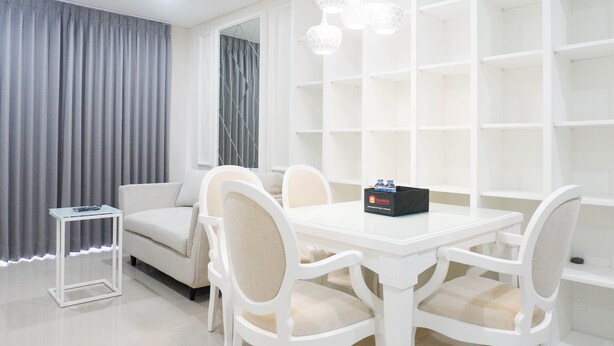 A modern dining area with a white table and chairs, a small side table, and a decorative light fixture. - Spacious 1BR Apartment at Praxis (Surabaya)