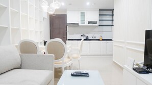 A modern living room with a sofa, a coffee table, and a TV. A kitchen with white cabinets and a dining area is visible in the background. - Spacious 1BR Apartment at Praxis (Surabaya)