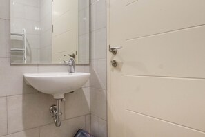 A bathroom with a white sink, a mirror, and a door. - Best Value 1BR Apartment Connected to Mall at Anderson Supermall Mansion (Surabaya)