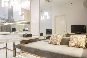 A modern hotel room with a sofa, a TV, a mirror, and a kitchenette area. - Best Value 1BR Apartment Connected to Mall at Anderson Supermall Mansion (Surabaya)