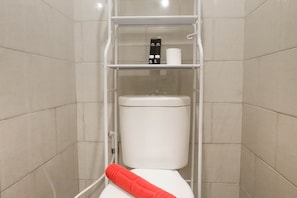 Une salle de bain avec des toilettes blanches, une serviette rouge et une étagère contenant des articles de toilette.