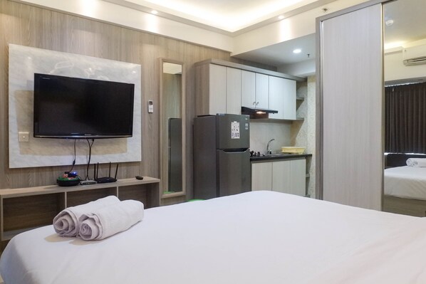 Une chambre d’hôtel dotée d’un grand lit, d’un téléviseur à écran plat fixé au mur, d’un réfrigérateur, d’une petite kitchenette et d’un espace nuit séparé.