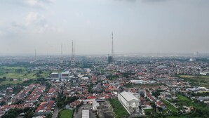 A cityscape with residential buildings, a large white building, and several tall communication towers. - Modern Luxurious Studio Apartment at Tanglin Tower Supermall Mansion (Surabaya)