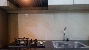 A kitchen with a gas stove, a sink, and a modern backsplash. - Modern Luxurious Studio Apartment at Tanglin Tower Supermall Mansion (Surabaya)