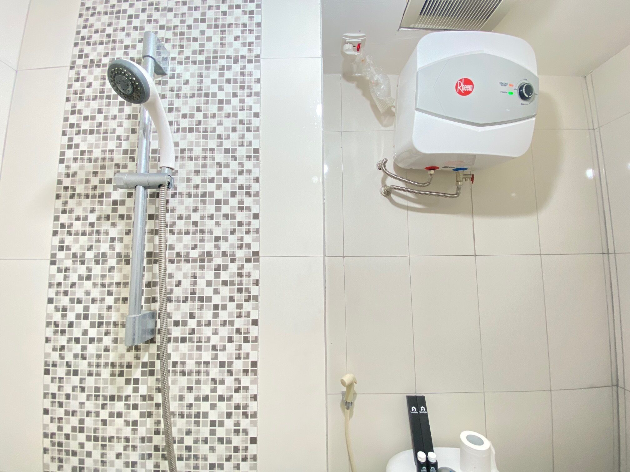 Une douche avec un mur recouvert de mosaïques, des toilettes blanches dotées d’un panneau de commande et un sèche-mains.