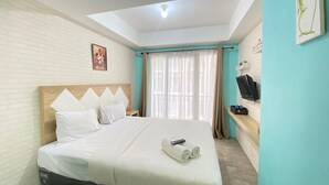 A hotel room with a bed, a TV, a painting, and a window with curtains. - Modern and Comfy Studio Room at Grand Asia Afrika Apartment (Bandung)