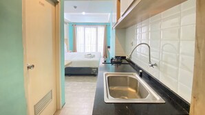 A compact hotel room with a kitchenette, a bed, and a bathroom. - Modern and Comfy Studio Room at Grand Asia Afrika Apartment (Bandung)