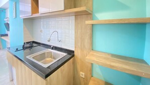 A kitchen with a black countertop, a stainless steel sink, and wooden cabinets. - Modern and Comfy Studio Room at Grand Asia Afrika Apartment (Bandung)